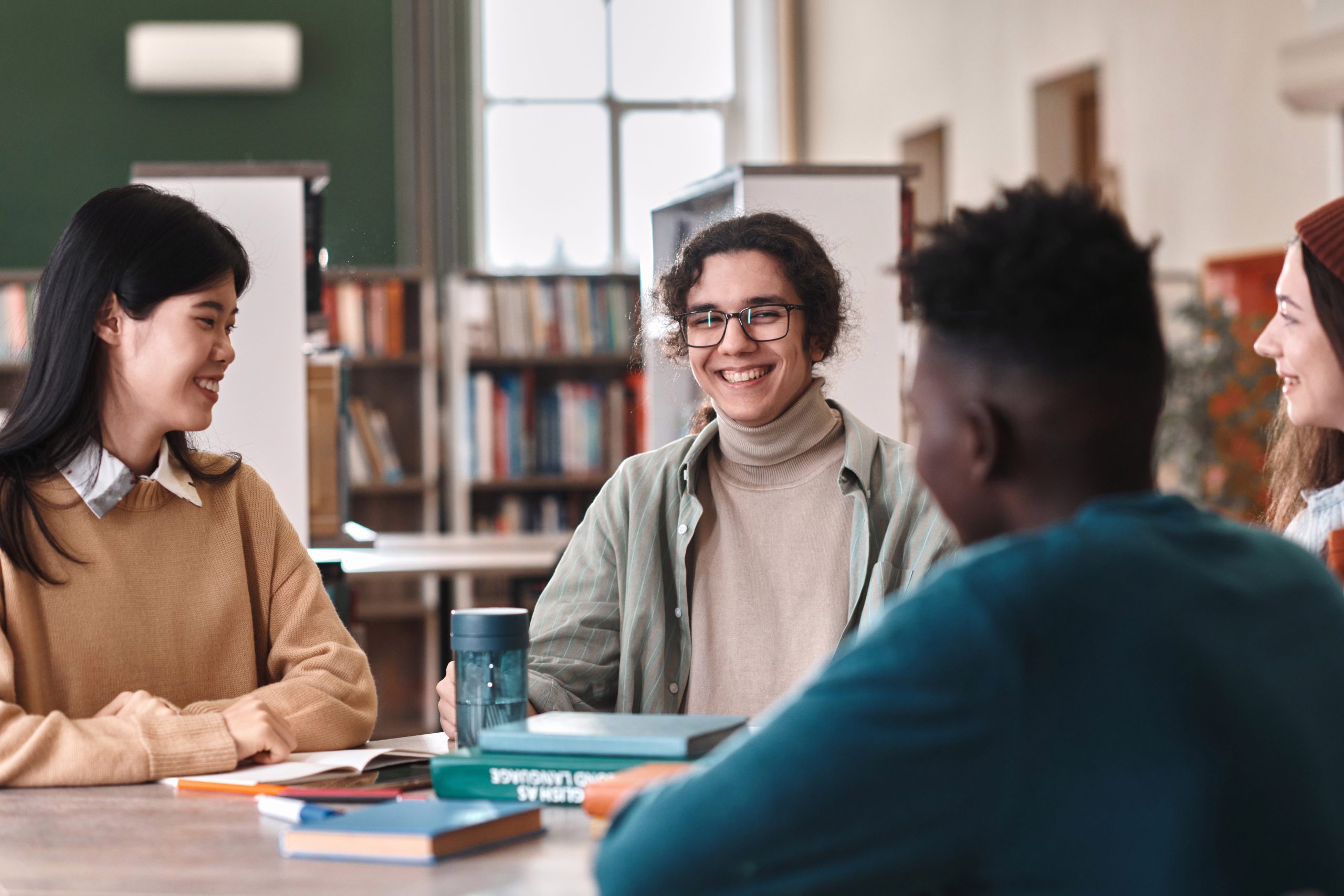 jeunes personnes discutent et rient autour d'une table de travail dans une bibliothèque
